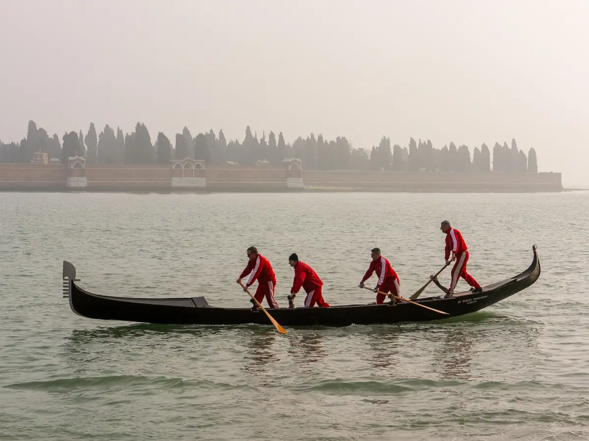 Four rowers standing in a gondola on the lagoon